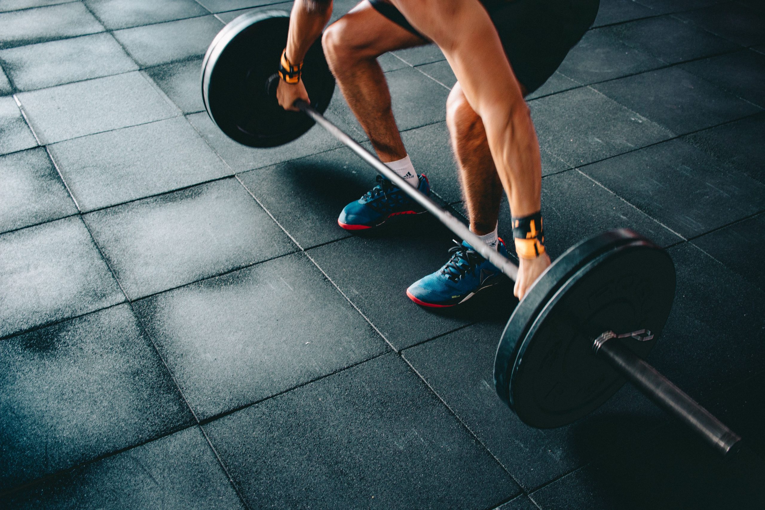 Deportista levantando una barra con discos en el suelo oscuro de un gimnasio
